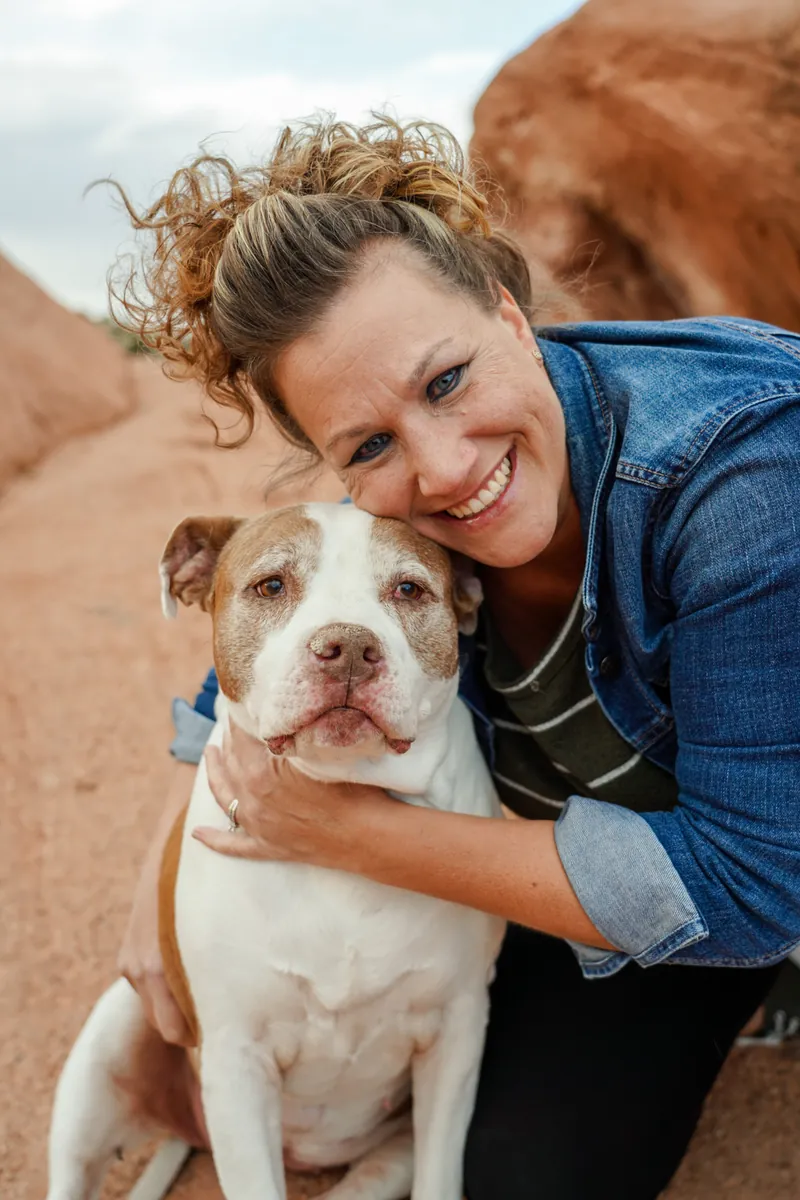Dr. Kim Bland smiling outdoors with her arms around her dog
